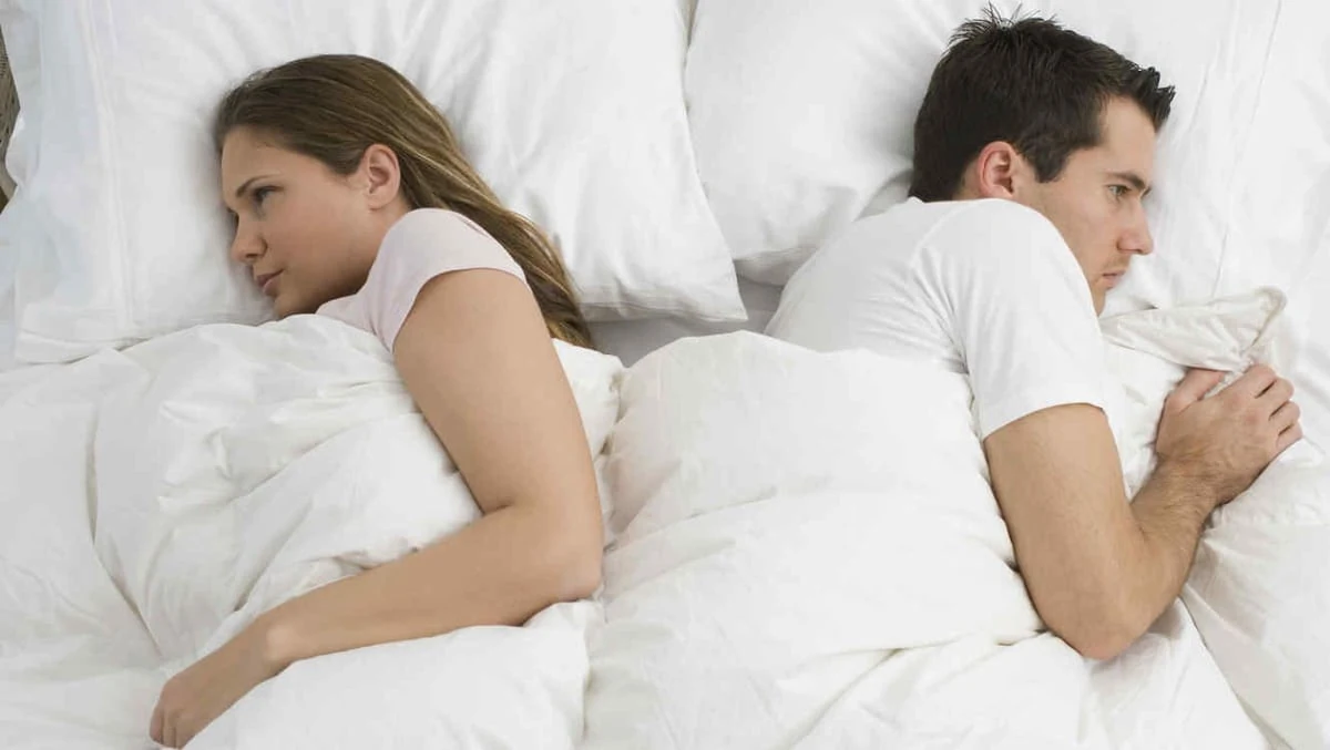 Mujer y hombre pensativos, acostados en la cama, simbolizando falta de deseo sexual