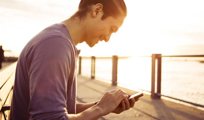 hombre joven con su celular en la mano mirando su pantalla y buscando algo