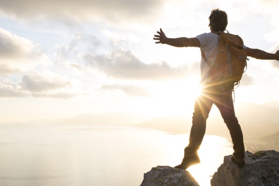 Persona alcanzando la cima de una montaña al amanecer, simbolizando motivación y superación personal.