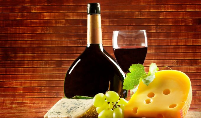 Botella y copa de vino tinto con uvas y queso sobre mesa rústica