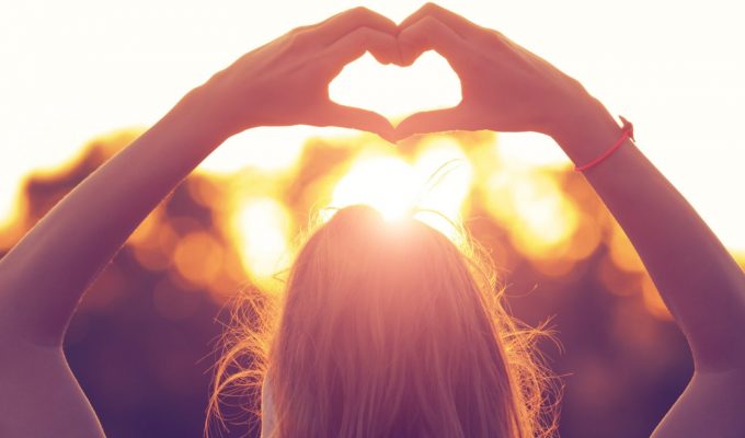 Mujer formando un corazón con las manos frente al sol, símbolo de amor por la naturaleza y estilo de vida eco-friendly.