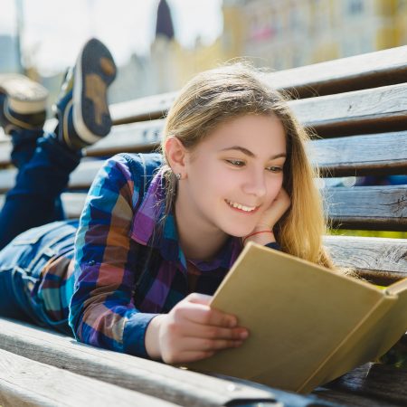 Mujer joven leyendo un libro con expresión de felicidad y disfrute.