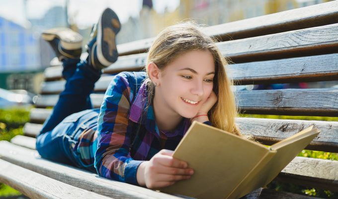 Mujer joven leyendo un libro con expresión de felicidad y disfrute.