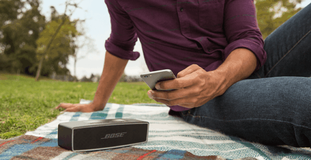 Hombre escucha música en un parque con un parlante Bluetooth y su teléfono móvil.