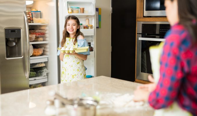 Niña sonriente sacando huevos del refrigerador en la cocina de su casa