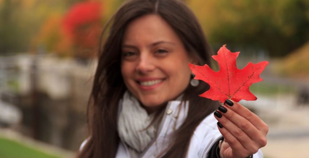Mujer hispana sonriente sosteniendo una hoja de arce roja, representando la esperanza y las oportunidades para profesionales en Canadá.