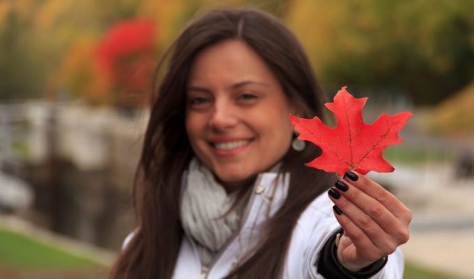 Mujer hispana sonriente sosteniendo una hoja de arce roja, representando la esperanza y las oportunidades para profesionales en Canadá.