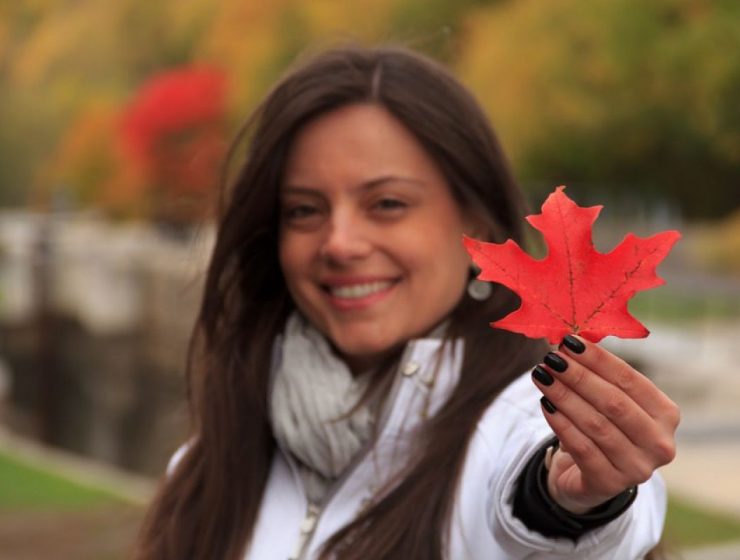 Mujer hispana sonriente sosteniendo una hoja de arce roja, representando la esperanza y las oportunidades para profesionales en Canadá.