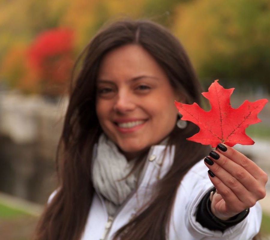 Mujer hispana sonriente sosteniendo una hoja de arce roja, representando la esperanza y las oportunidades para profesionales en Canadá.
