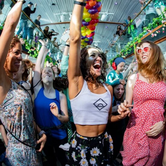 Personas bailando bajo una esfera disco en un evento Daybreaker en interior.