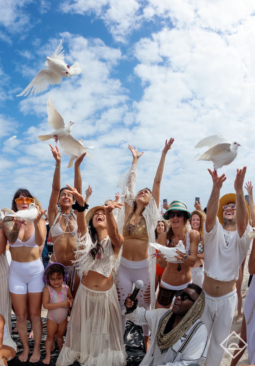 Personas vestidas de blanco soltando palomas al amanecer durante un Daybreaker. 