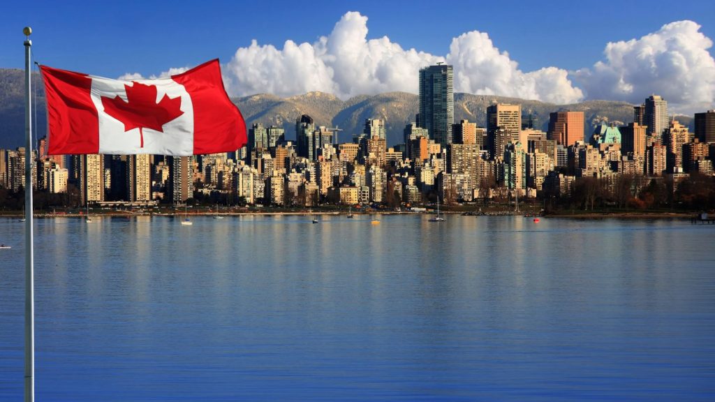 Bandera de Canadá ondeando con el skyline de Vancouver y las montañas de fondo, simbolizando oportunidades laborales e inmigración.