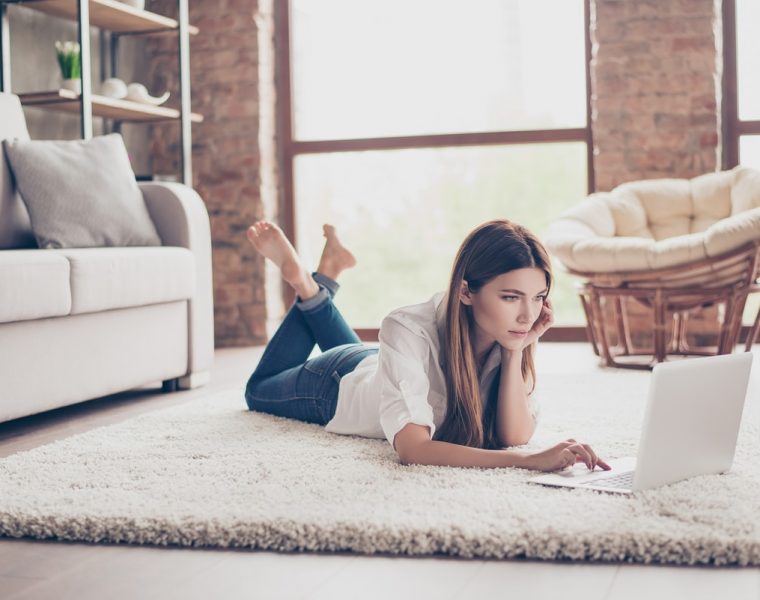 Mujer acostada revisando perfiles en redes sociales desde su computadora portátil.
