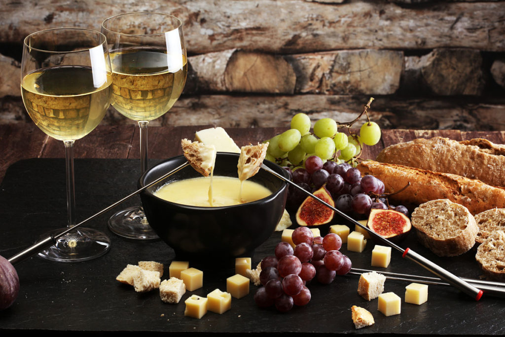 Fondue de queso con pan, uvas, higos y copas de vino blanco