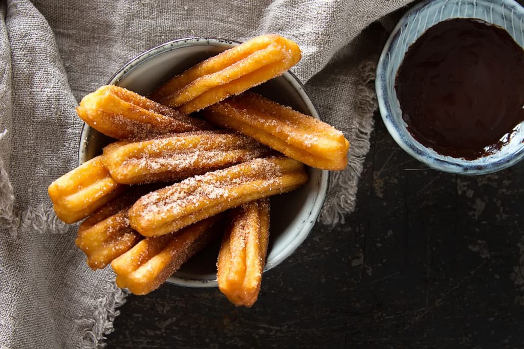 Tazón de churros espolvoreados con azúcar al lado de salsa de chocolate
