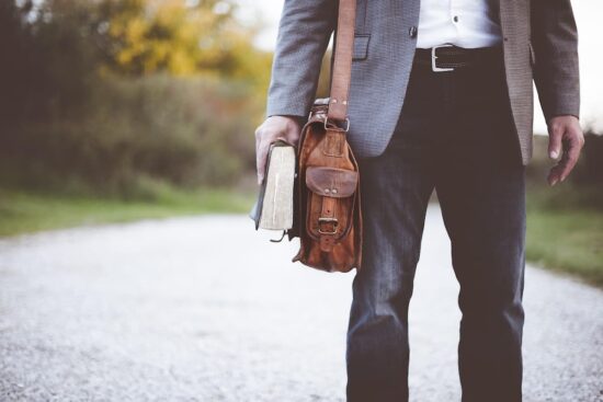hombre elegante con saco, jean y camisa blanca, con bolso de cuero y cinturón de cuero, con libro en su mano
