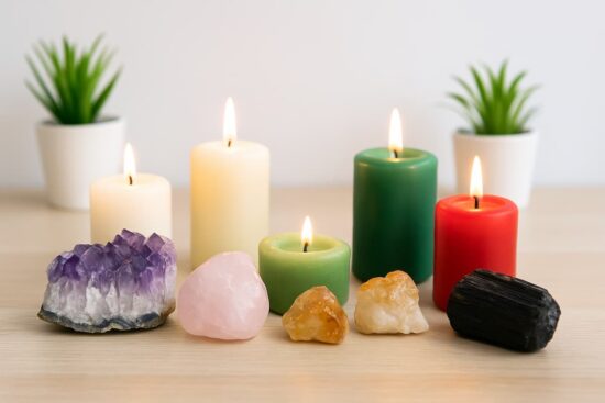 Cristales de amatista, cuarzo rosa, citrino y turmalina negra frente a velas encendidas de colores blanco, verde y rojo sobre mesa de madera clara.