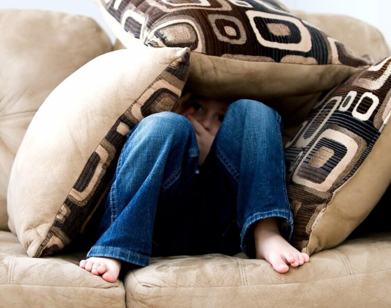 Niño escondido entre cojines en un sillón por miedo.