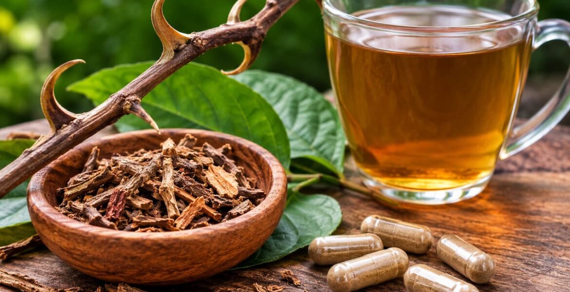 Uña de gato en corteza junto a una infusión herbal y cápsulas sobre una mesa de madera.