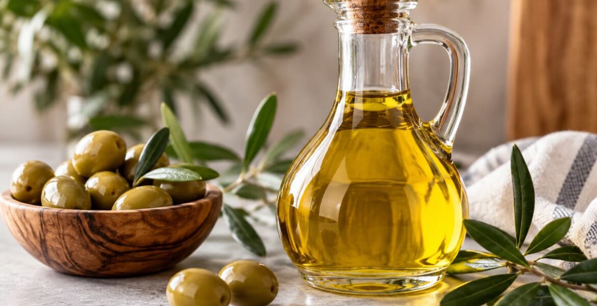 Aceite de oliva en botella de vidrio junto a aceitunas y ramas de olivo