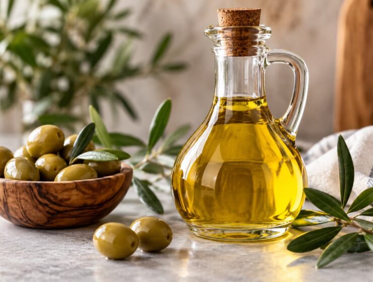 Aceite de oliva en botella de vidrio junto a aceitunas y ramas de olivo