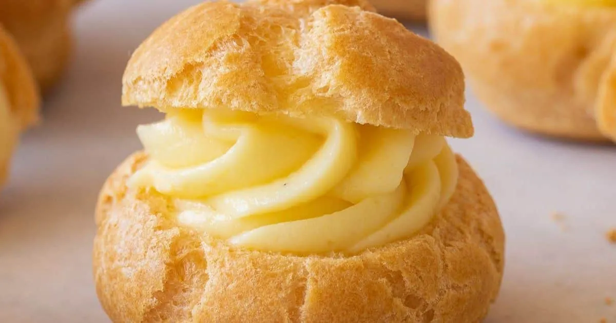 Profiterol relleno con crema pastelera, con masa dorada y textura esponjosa sobre fondo claro.