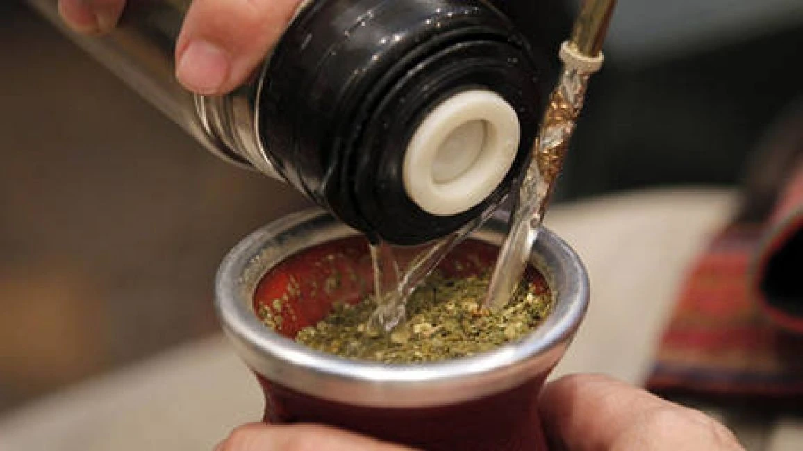 Termo sirviendo agua caliente en un mate con yerba y bombilla.