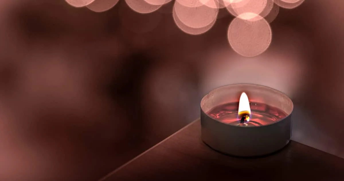 Pequeña vela encendida en un recipiente metálico con luces rosadas desenfocadas al fondo