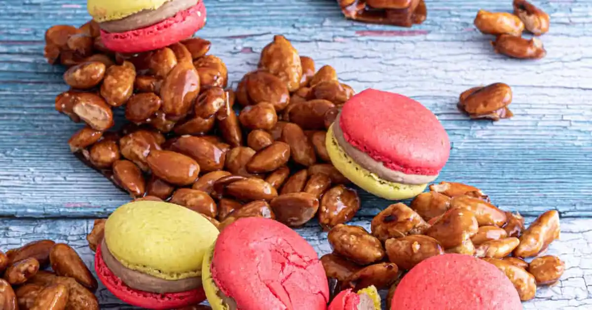 Garrapiñada de cacahuetes y almendras junto a macarons rosas y verdes sobre madera azul