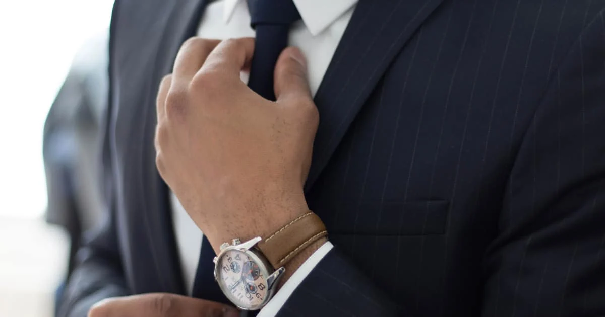 Primer plano de un hombre de negocios ajustando su corbata, mostrando un look profesional y la importancia de los detalles al combinar camisa y traje.