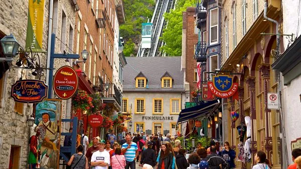 Calle concurrida de Petit Champlain en Quebec, con letreros en francés y el funicular al fondo. Destaca oportunidades de trabajo francófonas en Canadá.