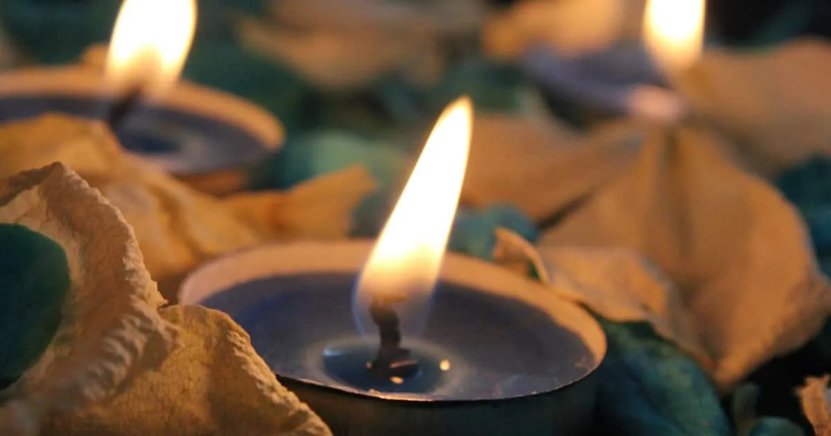 Velas pequeñas encendidas entre pétalos secos y piedras decorativas de color turquesa
