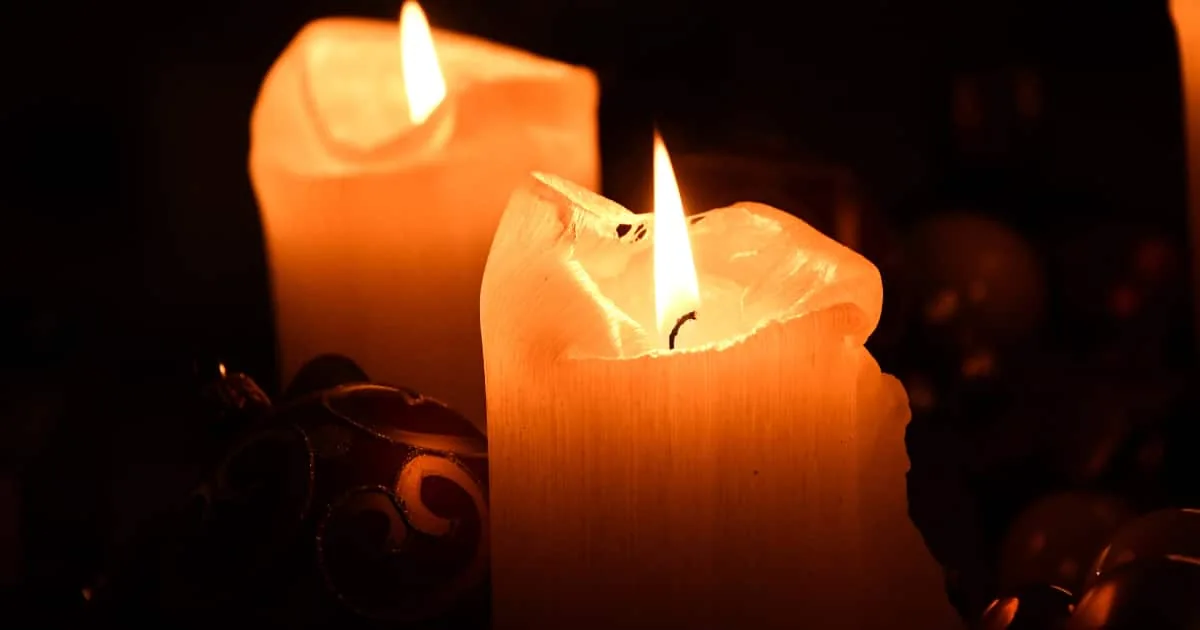 Dos velas anaranjadas encendidas con adornos navideños desenfocados al fondo