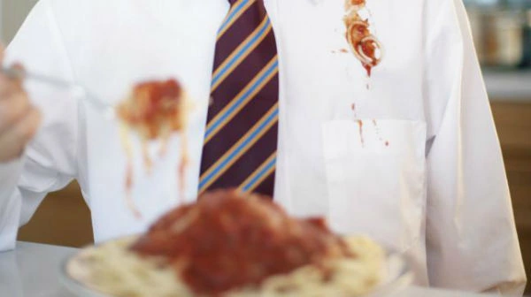 Las manchas de salsas en ropas de colores claras son las más rebeldes. hombre comiendo pastas con camisa y corbata con grandes manchas de salsa en sus prendas