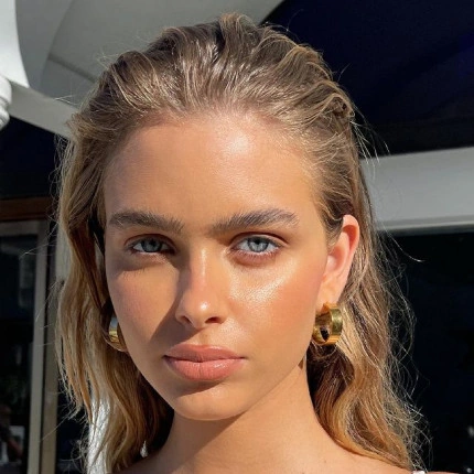 Modelo al aire libre con maquillaje natural y aretes dorados de aro