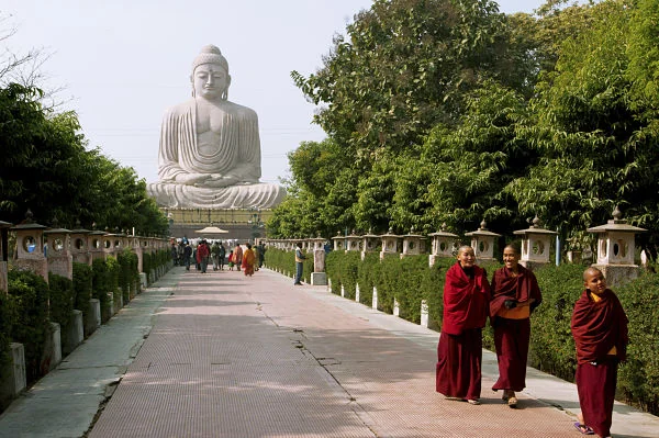 Monjes budistas frente a la Gran Estatua de Buda Monjes budistas con túnicas rojas caminando hacia una gran estatua de Buda en un entorno natural y sereno.