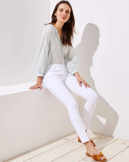 Mujer modelando un look de primavera con un pantalón blanco de corte 'skinny' y una blusa vaporosa de color verde menta pastel, complementado con sandalias planas color mostaza.