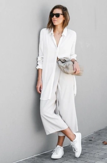 Mujer luciendo un look minimalista y monocromático, combinando un pantalón culotte blanco con una camisa larga a juego y tenis blancos.