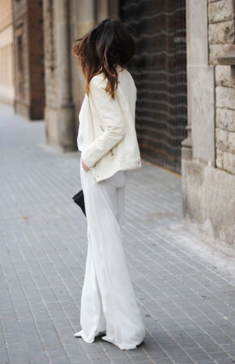 Mujer luciendo un elegante look monocromático con pantalón palazzo blanco, top a juego y una chamarra de piel o biker jacket en color crema.