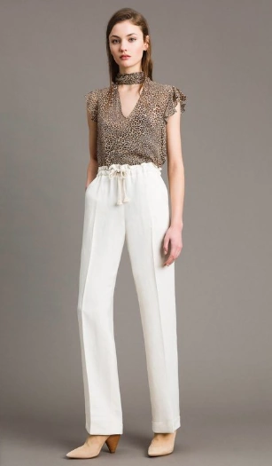 Modelo luciendo un outfit elegante al combinar un pantalón blanco de cintura alta tipo 'paper bag' con una blusa de 'animal print' de leopardo y botines nude.