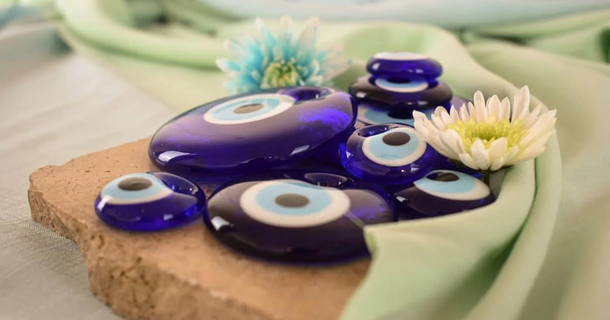 Ojo turco amuleto protector contra la envidia Amuletos de ojo turco azul sobre tela verde claro con flores decorativas.