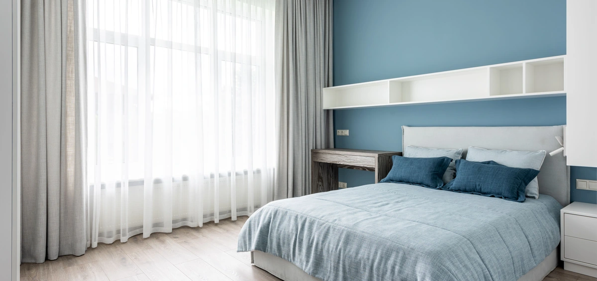 Dormitorio luminoso con una paleta de colores en tendencia: pared azul suave combinada con blanco, gris y madera, creando un ambiente de calma y relax.