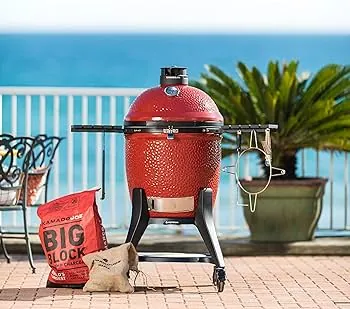 La navaja suiza de los asadores: asa, ahúma y hornea. Asador de cerámica Kamado Joe rojo en una terraza con vista al mar, un equipo versátil para asar y ahumar.
