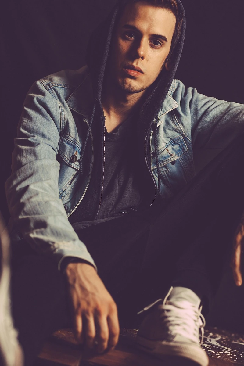 Domina el Arte del Layering Casual. Joven con estilo urbano vistiendo una chamarra de mezclilla sobre una sudadera con capucha, un ejemplo de look casual moderno para hombre.