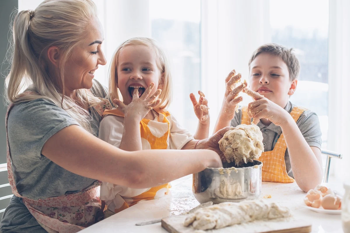 Madre cocinando con sus hijos, amasando masa juntos y riendo en la cocina.