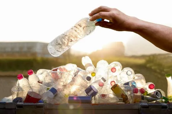 El Reciclaje de Plástico: Botella por Botella Depositando una botella de plástico en un gran contenedor de reciclaje lleno de otros envases
