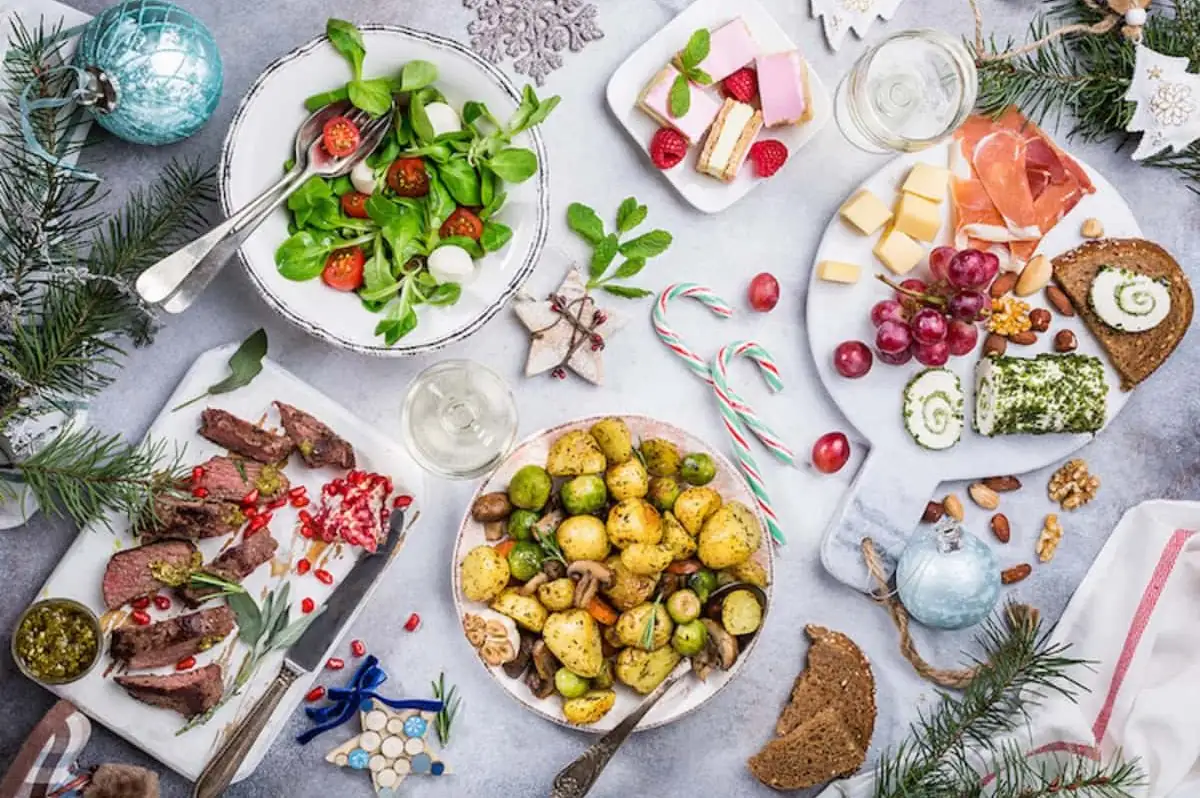Mesa decorada con comida navideña: ensaladas, carne asada, papas al horno y postres.