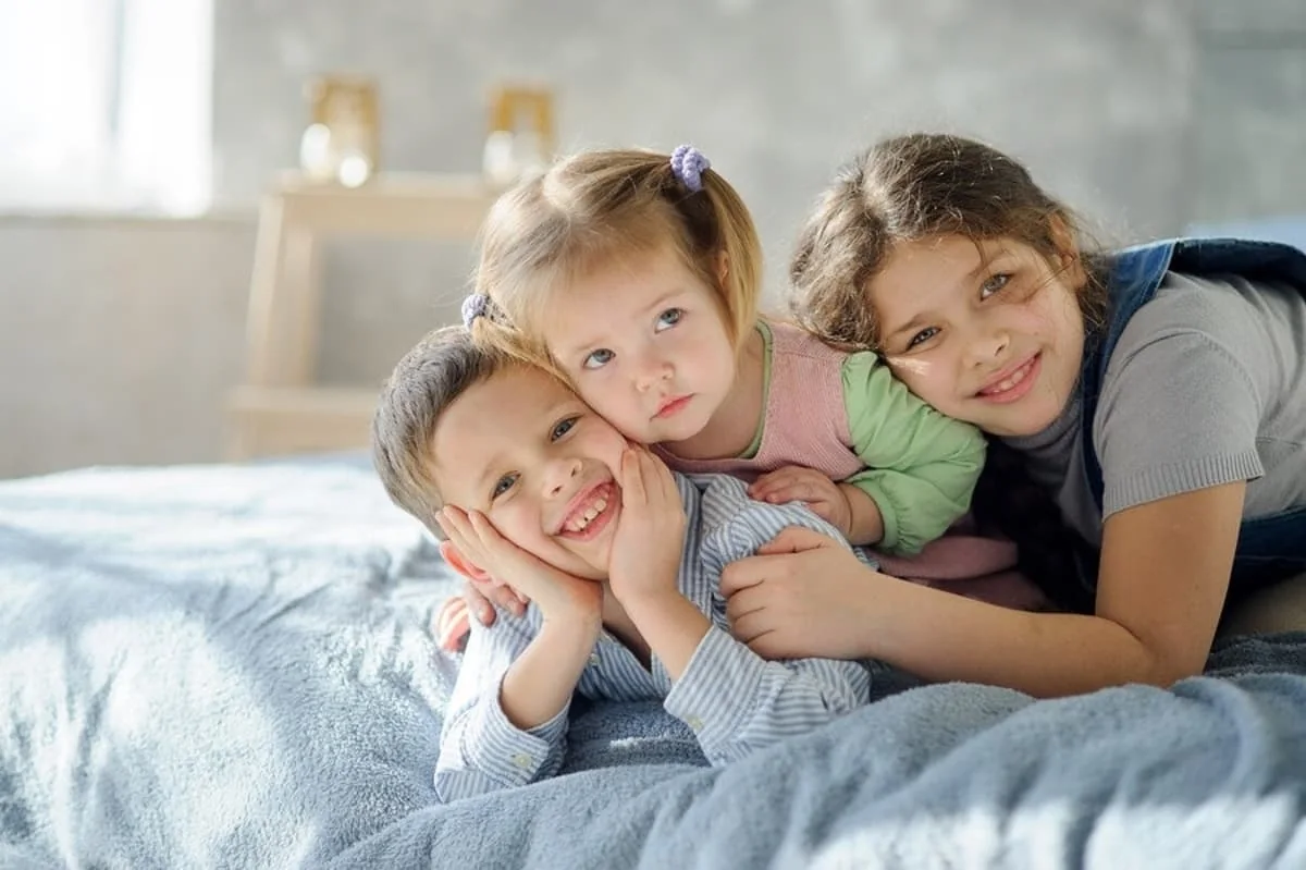 Fotografía de tres niños abrazados sobre una cama, reflejando la ternura, cercanía y complicidad entre hermanos.