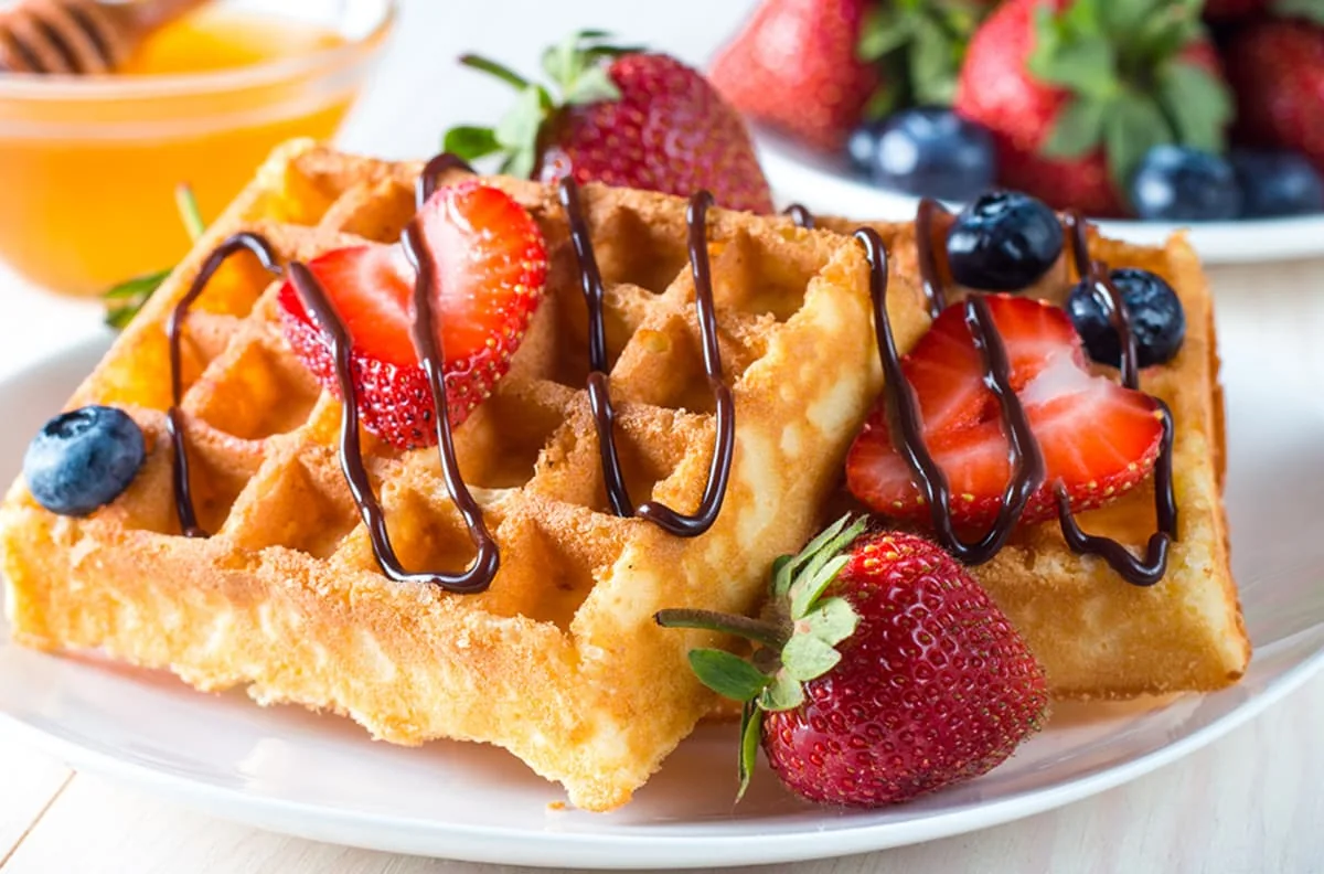 Waffles caseros dorados con fresas y arándanos frescos, decorados con chocolate derretido. Una receta deliciosa y fácil para un desayuno perfecto o brunch irresistible.