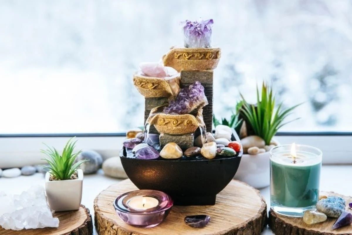Fuente decorativa con cristales, velas y plantas sobre una mesa de madera.